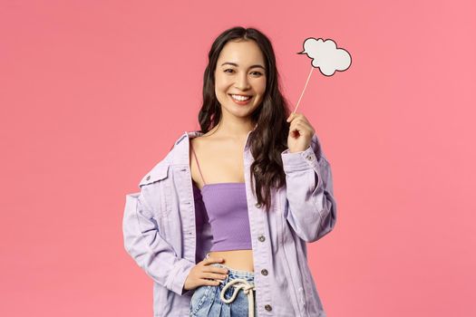 Holidays, lifestyle and people concept. Portrait of creative charismatic young asian girl in stylish outfit holding a cloud stick, comment, imaging something, having lots ideas, smiling pleased.