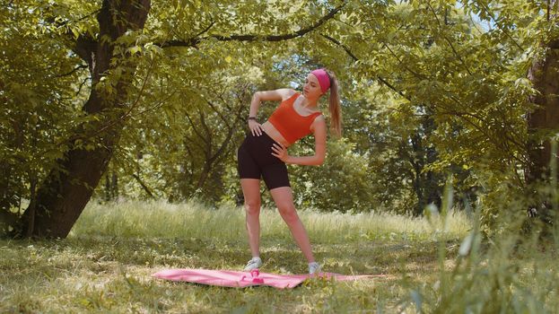 Sporty young woman doing stretching fitness tilts exercises outdoors in park. Slim athletic girl workout at sunny day. Female active athlete sportswoman in sportswear training. Healthy lifestyle