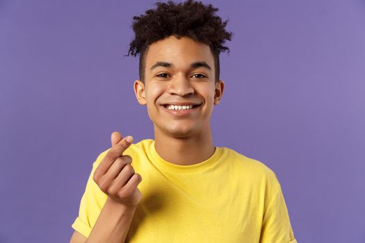 Lovely young romantic boyfriend, guy showing korean heart with fingers and smiling, like someone, being in love, show sympathy, standing purple background grinning upbeat.