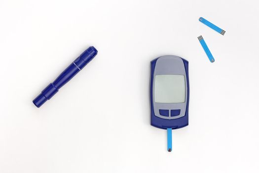 Top view of glucometer with blooded test strip inside and empty display, lancet and test strips on white background