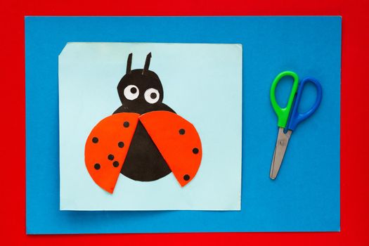 Top view of papercraft ladybug made by child and scissors on multicolor sheets background