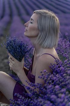 A middle-aged woman sits in a lavender field and enjoys aromatherapy. Aromatherapy concept, lavender oil, photo session in lavender.