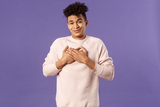 Portrait of touched silly young man left speechless and flattered, sobbing as being hit right into heart with dear warm words and praises, pleased standing purple background.