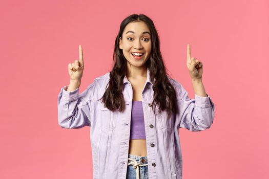 Lively attractive young brunette girl in denim jacket over crop-top asking you follow page, visit store or click link, recommend advertisement promo, smiling enthusiastic, pink background.