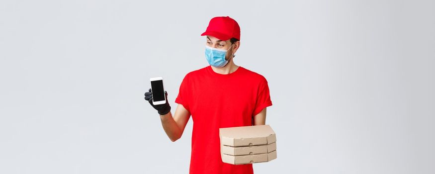 Food delivery, application, online grocery, contactless shopping and covid-19 concept. Surprised smiling courier in red uniform, holding pizza boxes and smartphone, showing app for bonuses or deliver.