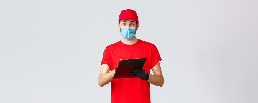 Packages and parcels delivery, covid-19 quarantine delivery, transfer orders. Enthusiastic courier in red uniform in face mask and gloves, writing down order adress, holding clipboard.