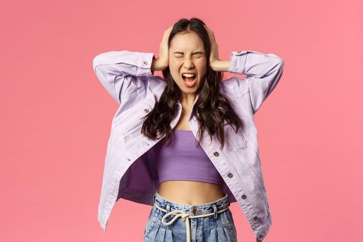 Portrait of depressed and uneasy, annoyed young girl pissed-off tired of hearing parents scoldings, shut ears and shouting with closed eyes, standing in denial, pink background.