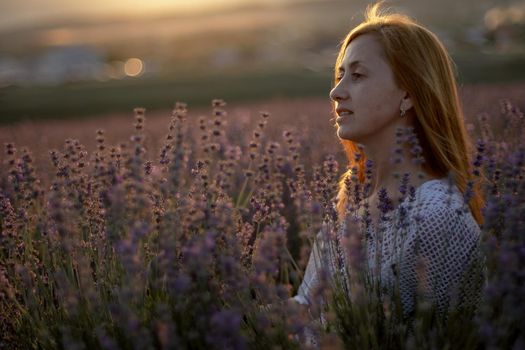 A middle-aged woman sits in a lavender field and enjoys aromatherapy. Aromatherapy concept, lavender oil, photo session in lavender.