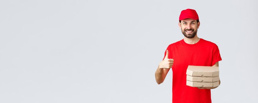Food delivery, quarantine, stay home and order online concept. Friendly smiling bearded courier in red uniform cap and t-shirt, recommend their service or restaurant, give pizza to customer.