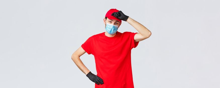 Covid-19, self-quarantine, online shopping concept. Delivery guy wiping sweat from forehead as tired of carry heavy packages to clients, working in coronavirus outbreak, wear face mask and gloves.