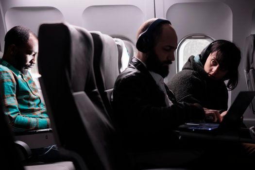 Young woman looking at man during airplane flight, using laptop online on aerial transportation. Group of tourists travelling by plane on international airline service, aviation jet.