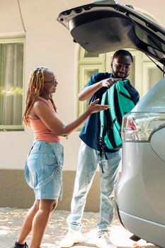 African american couple leaving on holiday trip with travel bags in automobile, loading suitcases in trunk. Man and woman travelling together by car to summer destination, vacation.