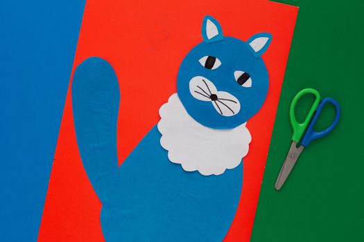 Top view of blue paper craft cat on red sheet and scissors