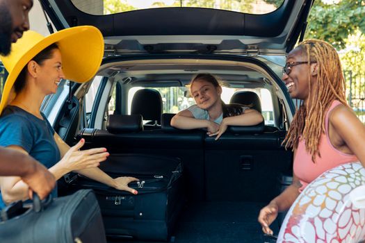 Multiethnic family and friends going on trip, loading baggage and inflatable in car trunk to travel to seaside. People preparing to leave on holiday vacation with luggage in automobile.