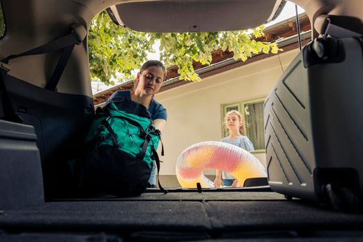 Mother and little girl loading baggage in car trunk, travelling on summer holiday trip. Putting inflatable and travel bags in automobile to leave on seaside adventure vacation.