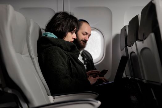 Young people travelling on holiday trip with aerial transportation, using laptop with online internet on commercial flight. Man and woman browsing computer on holiday destination, flying with plane.