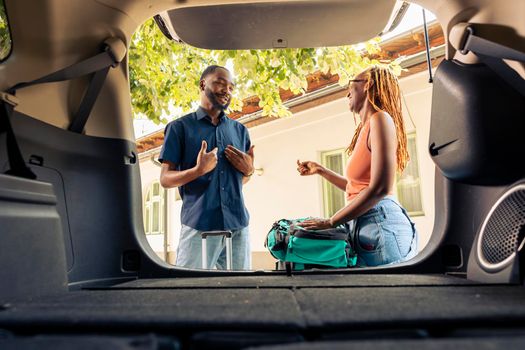 African american couple putting travel bags and trolley in trunk, getting ready to leave on holiday vacation with automobile. Travelling by car on road trip with luggage and suitcases.