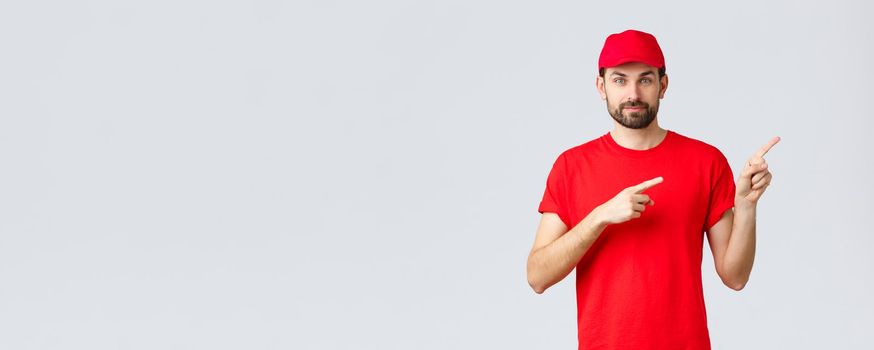 Online shopping, delivery during quarantine and takeaway concept. Confident bearded courier in red uniform cap and t-shirt, smiling camera, give direction, pointing finger right, inform clients.