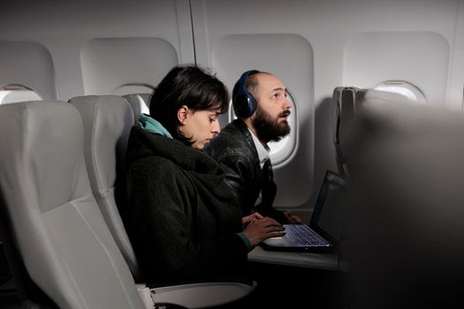 Woman working on laptop during airplane flight abroad, using online internet on computer to travel to holiday destination. Tourist waiting to arrive after commercial flight transportation trip.