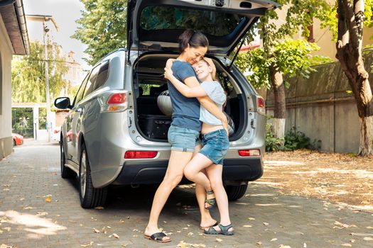 Mother and little girl hugging before travelling on holiday trip at seaside, loading luggage and suitcase in car trunk. Leaving on summer vacation with baggage and inflatable, leisure recreation.