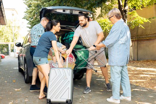 Relaxed people loading suitcase in trunk to travel on seaside vacation holiday, family preparing for adventure trip. Small child with parents and grandparents travelling with luggage during summer.