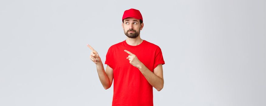 Online shopping, delivery during quarantine and takeaway concept. Uncertain and displeased, reluctant courier, employee in red t-shirt and cap, smirk disappointed pointing fingers upper left corner.