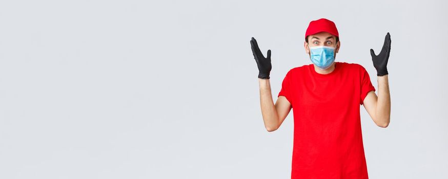 Covid-19, self-quarantine, online shopping and shipping concept. Surprised and confused delivery guy in medical mask, gloves and re duniform, shrugging, cant understand how it happened.