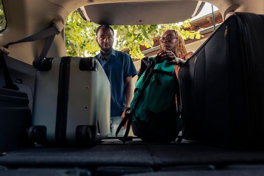 African american couple putting bags in trunk, travelling to holiday destination with luggage on road trip. Loading trolley and baggage in automobile to leave on summer vacation journey.