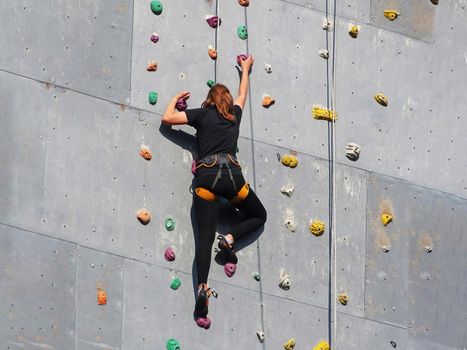 The girl is seen from the back in sportswear climbing in a sports climbing class. Adventure and Extreme Sport Concept