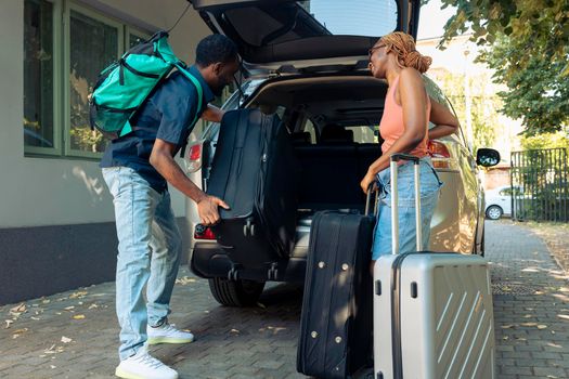 Boyfriend and girlfriend travelling on holiday, putting travel bags in trunk of automobile. Leaving on vacation trip for recreation. Couple in relationship going on urban adevnture with luggage.