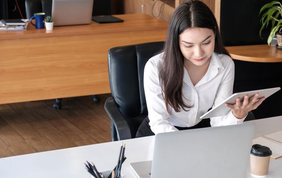 Young asian businesswoman works on tablet with laptop at the office..