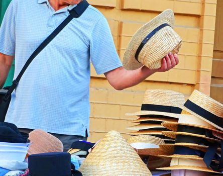 A customer is trying on hat with a headband. Man trying on a straw hat. Selling hats on the street