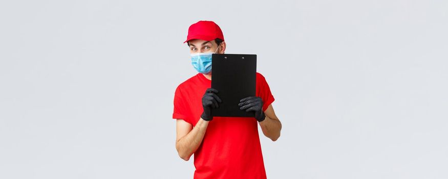 Packages and parcels delivery, covid-19 quarantine delivery, transfer orders. Friendly courier in carrier service bring order to doorstep, holding clipboard with sign form, wear face mask and gloves.