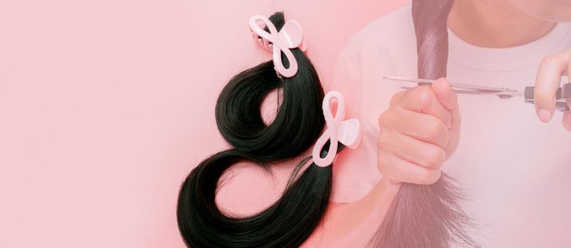 Hair donation for breast cancer person concept. Donate hair to wigs for breast cancer patients. Donate to cancer charity. Asian woman cutting long hair with scissors for donating on pink background.