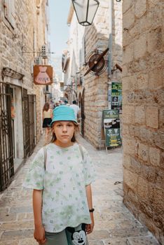 Girl tourist walking through ancient narrow street on a beautiful summer day in MEDITERRANEAN MEDIEVAL CITY , OLD TOWN bUDVA, MONTENEGRO. Young beautiful cheerful woman walking on old street at tropical town. Pretty girl looking at you and smiling