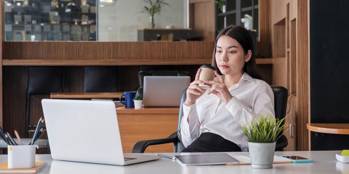 Asian businesswoman working using tablet holding coffee in the office..