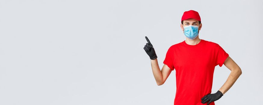 Covid-19, self-quarantine, online shopping and shipping concept. Delivery man in red cap and t-shirt, medical mask with gloves to protect clients and employees, pointing finger left at promo, show ad.