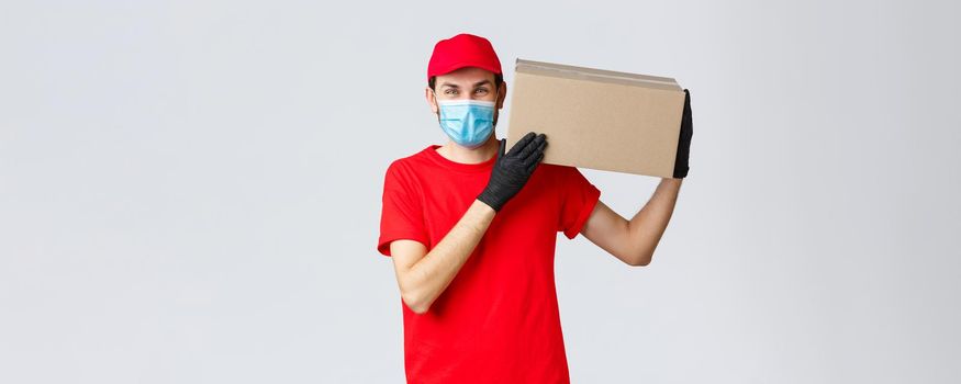 Packages and parcels delivery, covid-19 quarantine delivery, transfer orders. Friendly courier bring order to client house, holding package box on shoulder, wear face mask and rubber gloves.