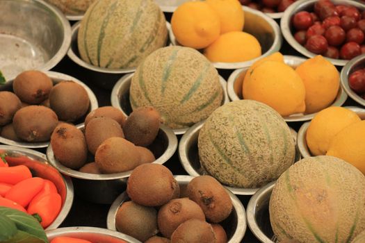 Fresh fruits on a market stall, kiwi, melons and lemons displayed in small metal bowls