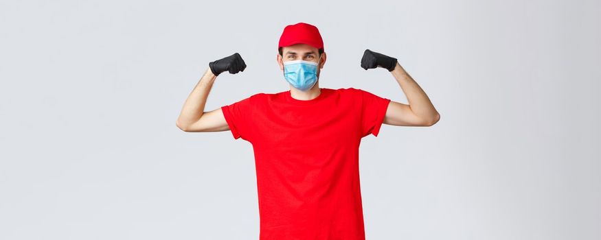 Covid-19, self-quarantine, online shopping concept. Strong delivery guy flexing biceps, showing strength, carry and transfer heavy large parcels to clients, express delivery to customer home.