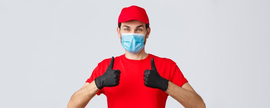 Contactless delivering, covid-19 and shopping concept. Cheerful courier or employee in face medical mask and gloves, show thumbs-up in approval, recommend using order shipping service.