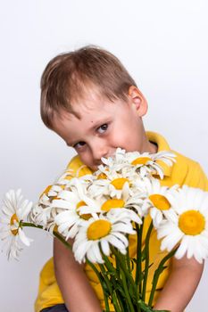 A cute boy with a beautiful bouquet of large daisies. Portrait of a child, funny and cute facial expression. Selective focus. A postcard for the celebration of the day of family, love and fidelity.