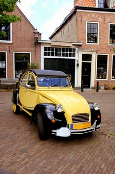 a vintage french car in yellow and black on a small village street