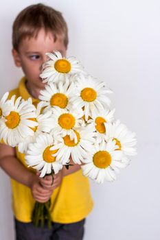 A cute boy with a beautiful bouquet of large daisies. Portrait of a child, funny and cute facial expression. Selective focus. A postcard for the celebration of the day of family, love and fidelity.