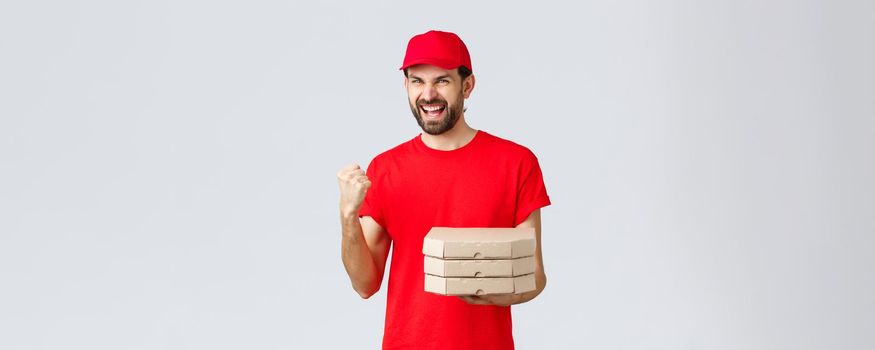 Food delivery, quarantine, stay home and order online concept. Enthusiastic courier in red t-shirt and cap, bring pizza orders to house, fist pump confident, winning celebrating victory.