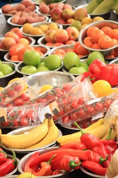 Fresh fruits and vegetables on a market stall: apples, bananas, peppers and other vegetables displayed in small metal bowls