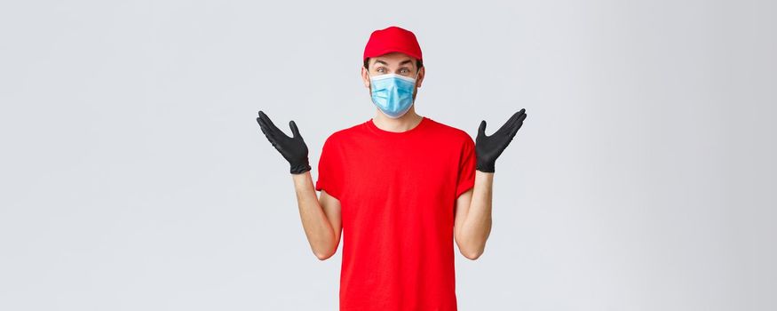 Groceries and packages delivery, covid-19, quarantine and shopping concept. Happy rejoicing delivery guy in red uniform, face mask and gloves receive good news, clap hands applause surprised.