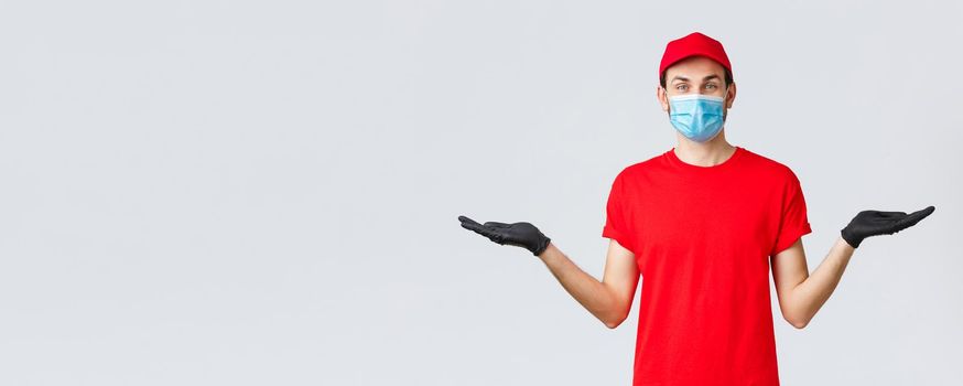 Groceries and packages delivery, covid-19, quarantine and shopping concept. Friendly delivery man in red uniform, face mask and gloves, holding two items or banners in hand, advice bonuses.