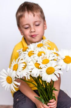 A cute boy with a beautiful bouquet of large daisies. Portrait of a child, funny and cute facial expression. Selective focus. A postcard for the celebration of the day of family, love and fidelity.