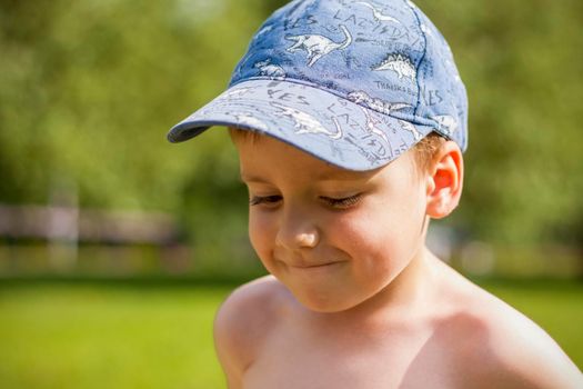 A cute blond boy experiences the joy of walking on a summer day by the river, sitting on the juicy grass. Funny facial expression. summer heat, a child without a T-shirt. Summer